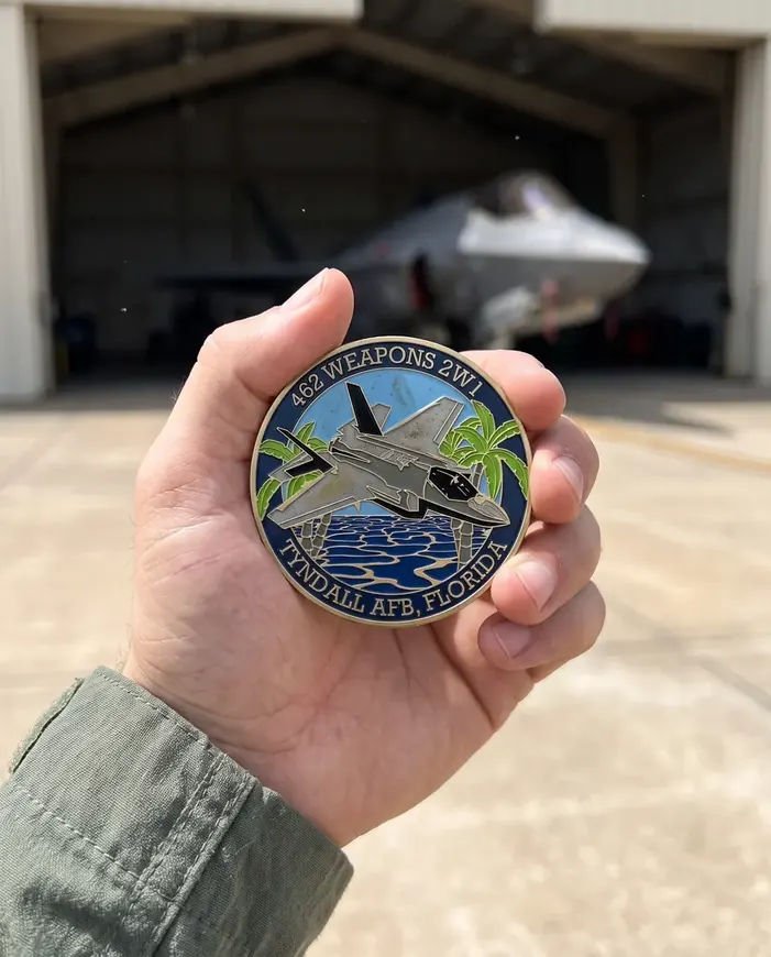 A 462 Weapons 2W1 Tyndall AFB coin held up in front of a hangar with an F-35