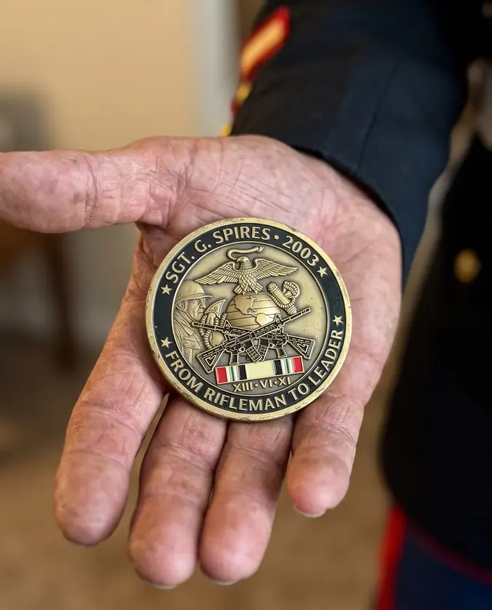 A personal Marine Corps coin, From Rifleman to Leader, in the open palm of a veteran in dress blues